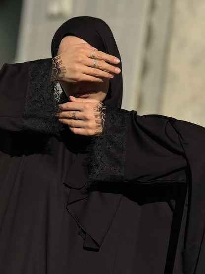 Elegante Vorderansicht der schwarzen Abaya Aswad Noir mit feinen Spitzendetails.