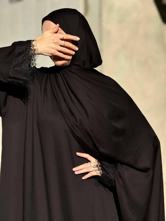 Elegante Vorderansicht der schwarzen Abaya Aswad Noir mit feinen Spitzendetails an den Ärmeln.