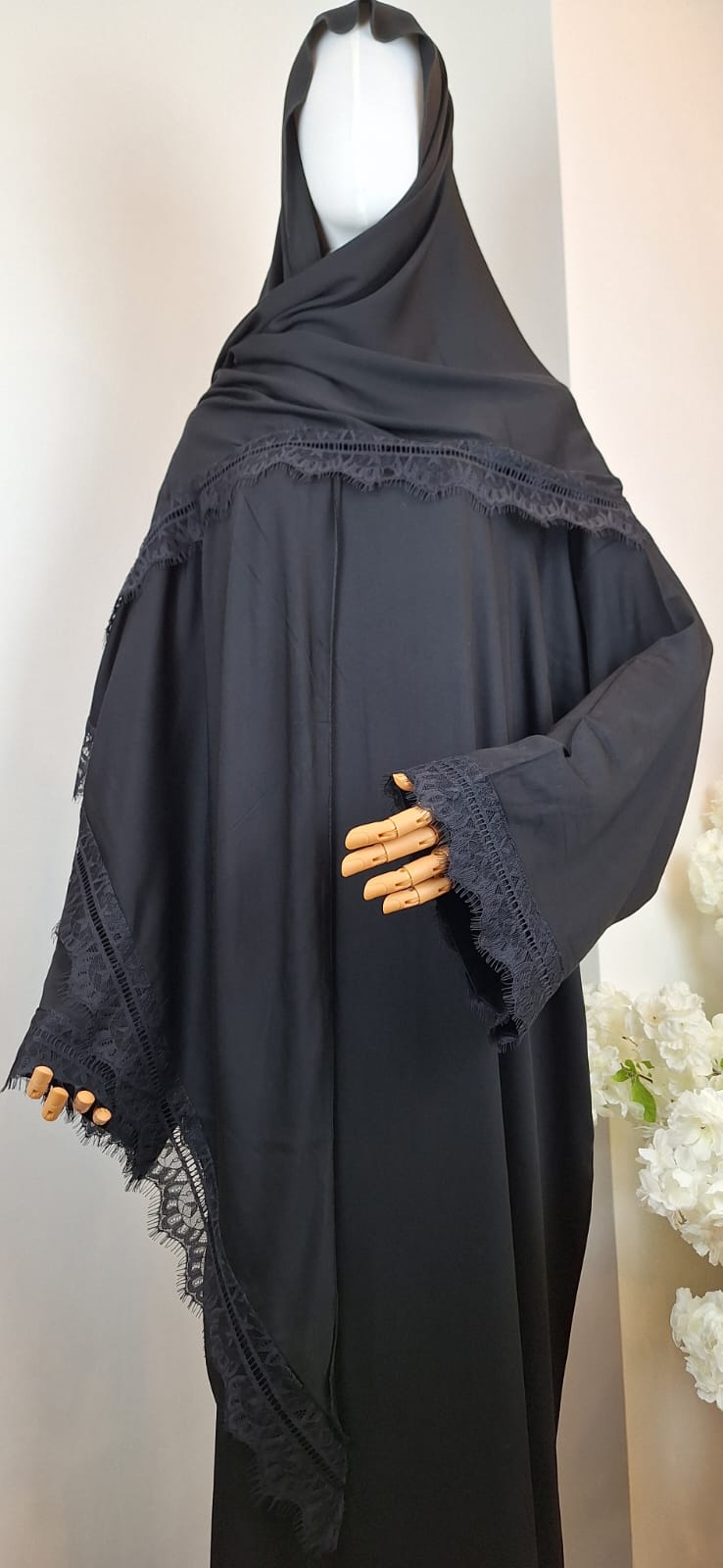 Moderne schwarze Abaya mit elegant drapiertem Kopftuch und feiner Spitzenbordüre entlang der Kante.