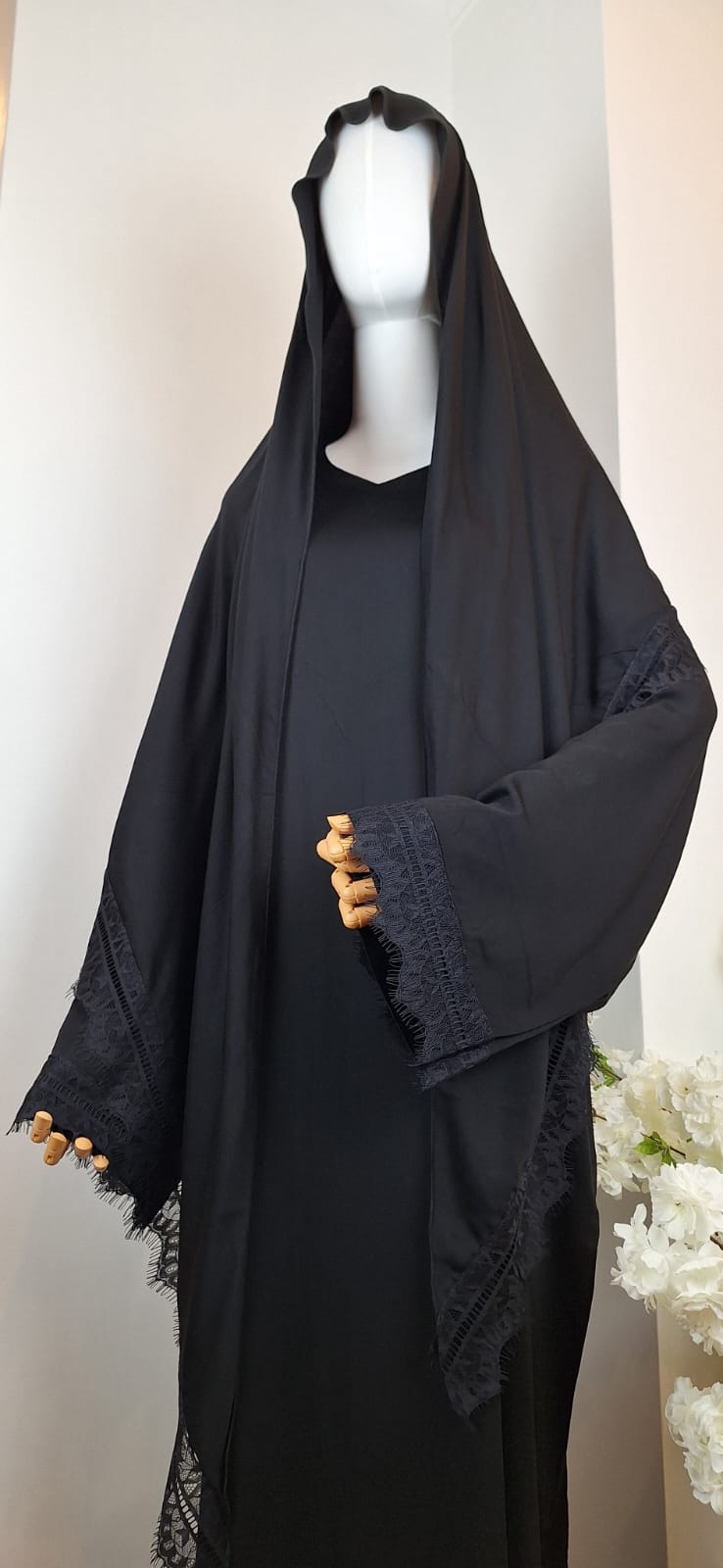 Schwarze Abaya „Aswad Noir“ mit locker fallendem Kopftuch und Spitzenbesatz an den Ärmeln – Frontansicht.